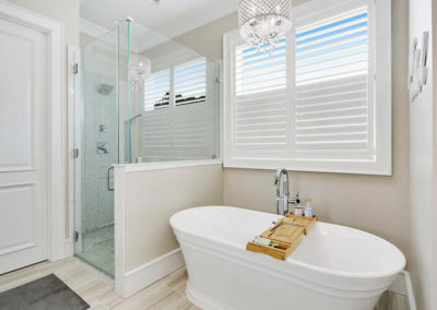 white faux wood interior shutters on bathroom window in front of stand alone tub