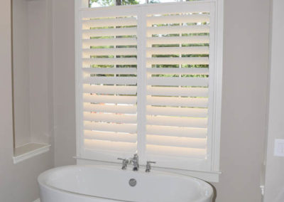 white faux wood interior shutters on bathroom window in front of stand alone tub