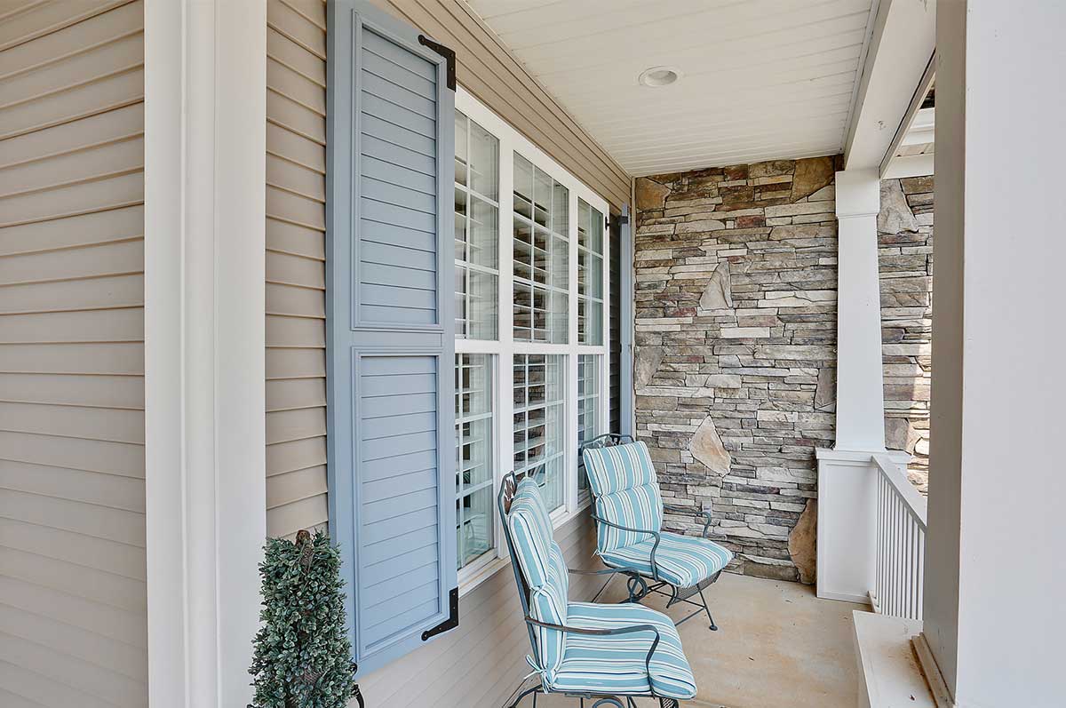 powder blue louvered shutters with black shutter hardware on house with tan siding and stone